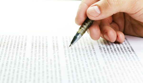 Close-up of male hand following text on paper with a pen